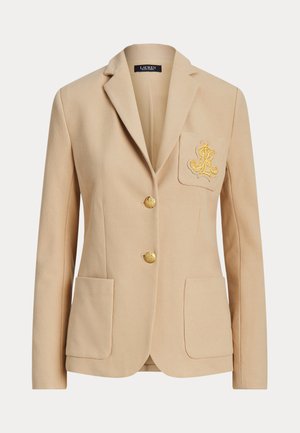 Blazer beige en tissu texturé, avec un design à un bouton, deux poches avant et un logo brodé en doré sur la poitrine.