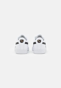 Fehér bőr sneaker cipők fekete csíkokkal és arany részletekkel a sarkán. Textúrált talp és domborított logó a hátsó részen.