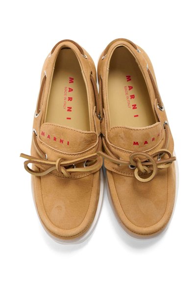 Mocassins Marni en daim beige avec nœuds sur le devant, œillets métalliques sur les côtés, et logo rouge Marni à l'intérieur et sur l'avant de la chaussure.