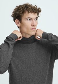 Mørkegrå turtleneck genser laget av mykt strikkemateriale, med lange ermer og ribbestrikket krage. Enkel, strukturert design.