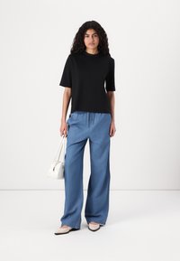 Haut noir à manches courtes associé à un pantalon large bleu clair, doté d'une taille élastique, complété par un petit sac à main blanc.