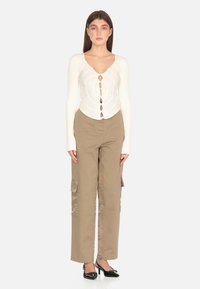 Maglietta bianca a righe con maniche lunghe, scollo a V e chiusura con bottoni, abbinata a pantaloni cargo kaki con tasche laterali e vestibilità comoda. Tacchi neri.