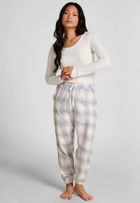 Crème top met lange mouwen gecombineerd met lichtblauwe en beige geruite broek, voorzien van een elastische tailleband en enkelfranden. Zachte stoftextuur.