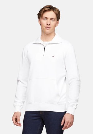 Sudadera blanca de media cremallera con un bolsillo frontal, que presenta un pequeño logo de la marca. Textura suave y puños acanalados en las mangas y el dobladillo.
