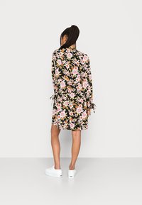 O vestido floral é preto com flores rosa e laranja, apresentando mangas longas e punhos atados. Usado com tênis brancos, tem um corte solto.