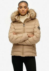 Beige dunjakke med hætte foret med pels, lynlås foran og vandret quiltning. Har et logo-patch på ærmet.