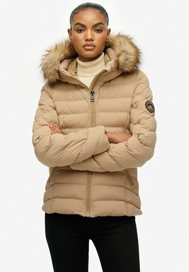 Beige dunjakke med hætte foret med pels, lynlås foran og vandret quiltning. Har et logo-patch på ærmet.