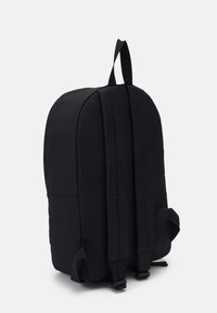 Sac à dos noir en tissu lisse, avec une forme arrondie, des bretelles rembourrées et une poignée de transport en haut. Design minimaliste sans logos visibles.