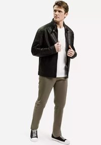 Czarna skórzana kurtka z pikowanymi detalami na ramionach, biała koszulka, oliwkowe spodnie i czarne sneakersy z białymi sznurówkami. Casualowy strój.