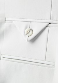 Valge kangas, millel on terav krae kolmnurkse lapiga, üks ümmargune nööp ning taskute ääres nähtav õmblus.