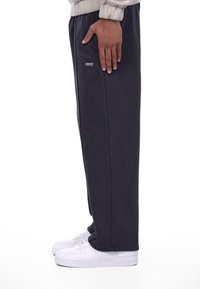 Mørkegrå sweatpants lavet af bomuldsblanding, med lige snit og sidelommer. Båret med hvide sneakers på en ensfarvet baggrund.