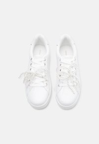 Baskets blanches présentant une tige synthétique lisse, des accents texturés et des lacets décoratifs semblables à des perles. Conception à bout arrondi.