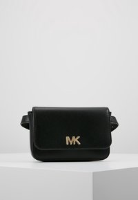 Bolso bandolera de cuero negro con cierre de solapa magnético, que cuenta con un logo "MK" en tono dorado y correa ajustable. Textura suave, diseño compacto.