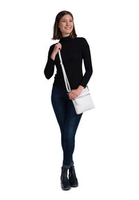 Hvid læder crossbody taske med en lynlåslomme, båret af en person i en tætsiddende sort top og mørke jeans, med en lang justerbar rem.