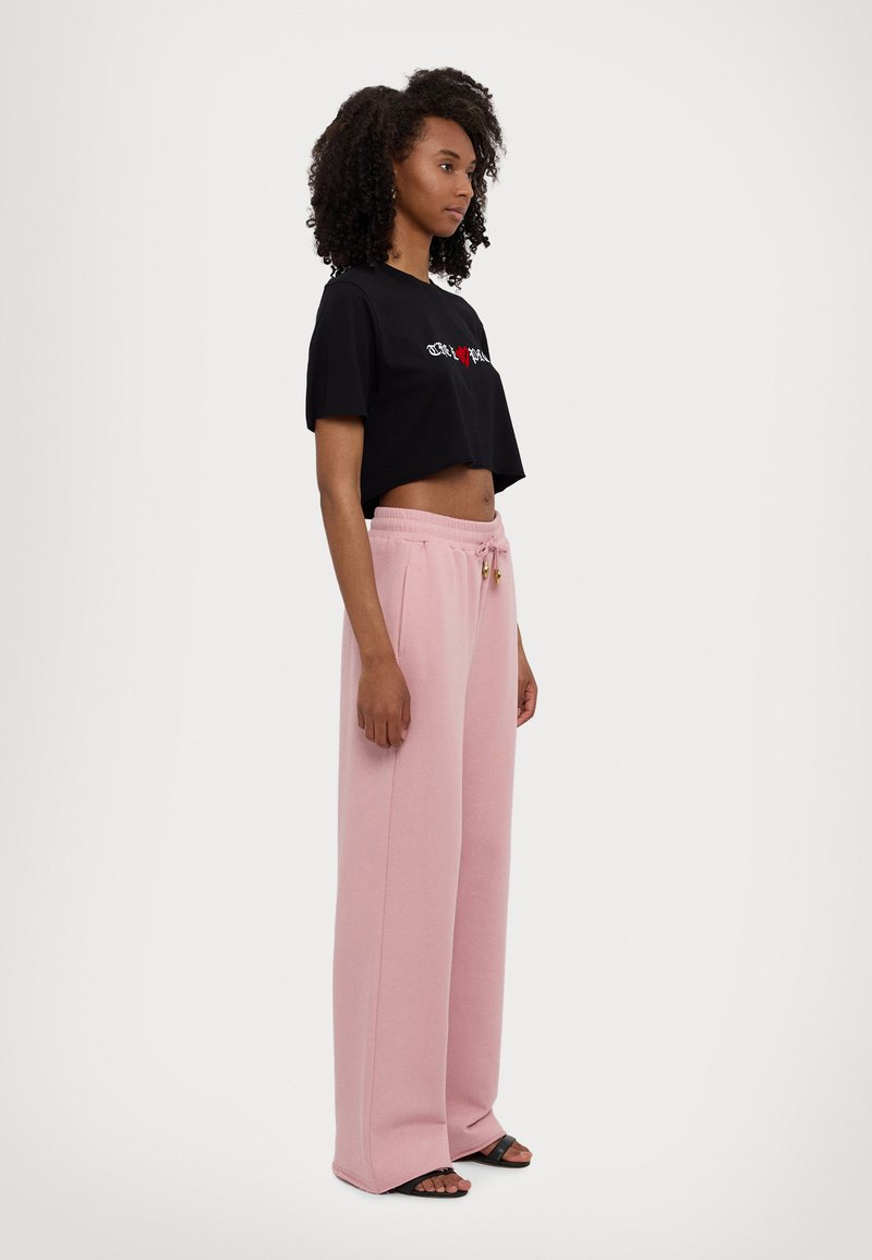 Sort cropped t-shirt med hvidt og rødt grafisk design, parret med lyserøde sweatpants med snøre og brede ben. Sandaler fuldender looket.
