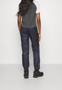 Svarta quiltade byxor med elastiska muddar och en grå kortärmad topp med randig design, sedd bakifrån.