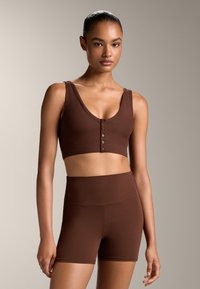 Un crop top marron à côtes avec un décolleté en V profond et une fermeture à boutons à l'avant, associé à un short marron taille haute, les deux présentant une texture lisse.