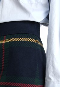 Gyapjú kockás szoknya, tengerészkék derékrésszel és zöld, piros, valamint sárga tartán mintázattal. Az anyaga puha, texturált felülettel rendelkezik.
