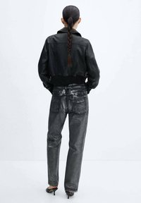 Chaqueta de cuero negra corta con dobladillo acanalado, combinada con jeans metálicos grises brillantes que cuentan con bolsillos traseros y diseño de pierna recta.