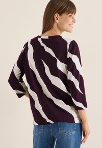 Top a maniche lunghe a righe viola e bianche con una vestibilità comoda e scollo rotondo, realizzato in un tessuto morbido, con audaci motivi asimmetrici.