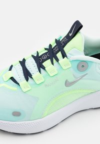 Baskets de sport Nike avec une tige vert menthe clair, en matériau mesh, des lacets bleu foncé et un logo swoosh gris. Le design comprend une semelle texturée.