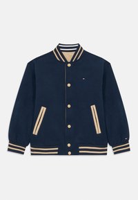 Navy blue varsity jacket made from soft fabric, featuring tan accents, striped collar, and button closures. Two side pockets with stripes.