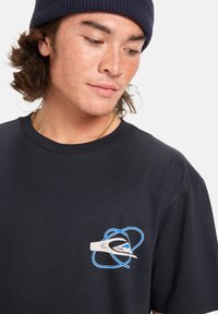 Tricou din bumbac negru cu un grafic mic multicolor pe pieptul stâng, gât rotund și mâneci scurte.