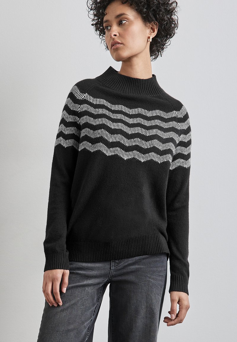 Schwarzer Pullover mit hohem Kragen, der ein Wellenmuster in Weiß über der Brust aufweist. Hergestellt aus einem weichen, strukturierten Stoff.