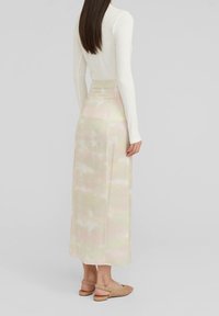 Kvinna i en lång pastellfärgad tie-dye kjol, vit långärmad topp och beiga vävda slingback skor, stående mot en enfärgad bakgrund.