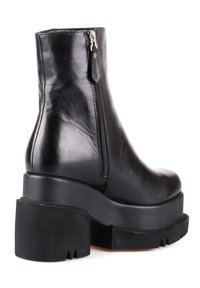 Stivale alla caviglia in pelle nera con zip laterale e suola piatta spessa. Presenta una texture liscia e un design con punta arrotondata.