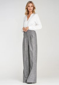 Biała bluzka z długim rękawem, dekoltem w serek i mankietami zapinanymi na guziki, w połączeniu z szarymi, w kratkę spodniami o wysokim stanie i szerokich nogawkach.