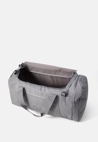 Sac de voyage gris avec une surface lisse et texturée. Il dispose de deux poignées, d'une ouverture zippée et d'un intérieur spacieux pour le rangement.