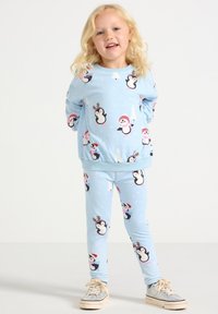 Light blue pajama set featuring repeated penguin and snowflake patterns. Sweatshirt with rounded neckline, elastic cuffs; fitted leggings.
