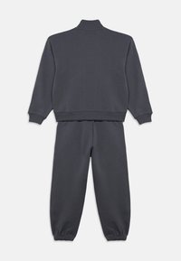 Czarnoszary dres wykonany z miękkiej bawełny. Posiada wysoki kołnierz, ściągacze na mankietach oraz elastyczny pas w spodniach. Prosty design bez wzorów.