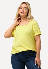 T-shirt giallo a maniche corte con scollatura quadrata e maniche arrotolate. Realizzato in un tessuto morbido e leggero, presenta una texture liscia.