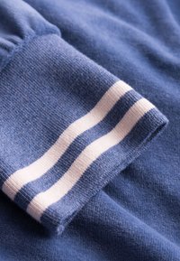 Blue sweatshirt fabric with a ribbed cuff featuring two white horizontal stripes. Soft texture with a smooth finish.