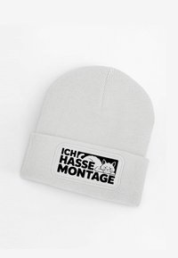 White knitted beanie featuring a black patch with the text "ICH HASSE MONTAGE" and a cat illustration. Soft texture, snug fit.