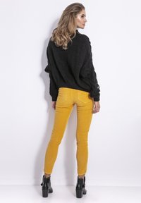 Gruby czarny sweter dzianinowy z detalami w warkocze, w zestawieniu z jasnobrązowymi skórzanymi spodniami skinny i czarnymi botkami na obcasie.