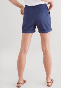 Navy blue cotton shorts with rolled cuffs, featuring back pockets and a smooth texture, worn with brown strappy sandals.