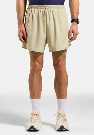 Light beige running shorts with an elastic waistband, featuring a grid texture and side pockets, worn over green compression shorts.