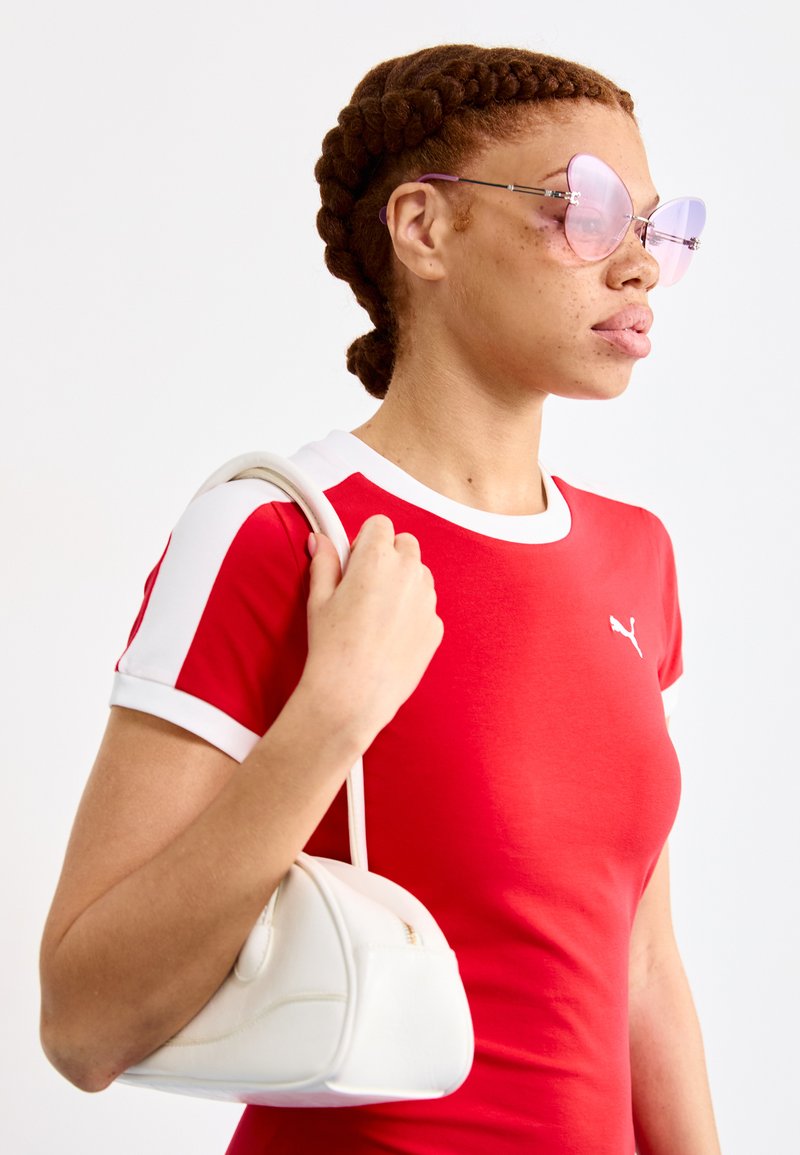 Camiseta roja ajustada con detalles blancos y logo, combinada con un pequeño bolso blanco. Grandes gafas de sol en tono rosa con forma de mariposa.