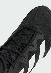 Musta urheilukengä, jossa on kuvioitu verkkopäällinen, nauhakiinnitys ja erottuva valkoinen geometrinen kuvio sivussa.