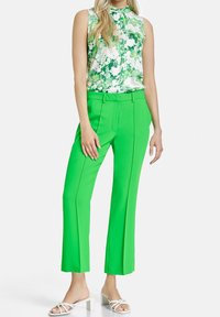 Zielona, bezrękawnikowa bluzka w kwiaty w połączeniu z jaskrawozielonymi szerokimi spodniami. Strój charakteryzuje się gładką fakturą i nowoczesnym krojem.