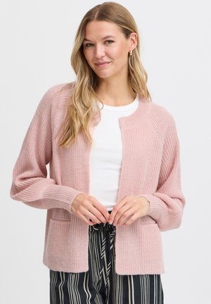 Gilet en tricot rose avec des manches longues, un devant ouvert et deux poches avant. Il présente des poignets côtelés et une coupe décontractée. Porté sur un haut blanc.