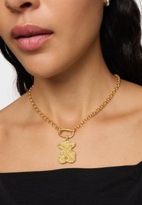Collana in oro con pendente a forma di orsetto testurizzato, caratterizzata da una robusta catena a maglie e un dettaglio di chiusura prominente.