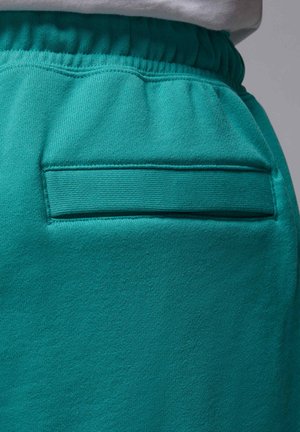 Hosen aus samtblauem Stoff mit elastischem Bund und einer waagerechten Schlitz-Detail an der Gesäßtasche, kombiniert mit einem weißen Oberteil.