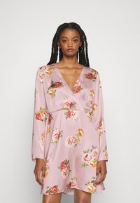 Vestido floral em cetim rosa claro, apresentando mangas longas, um decote em V profundo e uma saia rodada com padrões de flores coloridas por toda a peça.