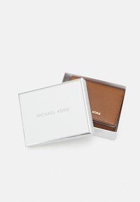 Smeđi kožni novčanik unutar bijele kutije Michael Kors. Novčanik ima teksturiranu površinu i ušiveni logotip marke u zlatnoj boji.