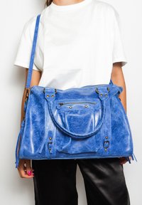 Borsa a mano in pelle blu con finitura texturizzata, doppi manici, tracolla regolabile e tasca con zip anteriore. Caratterizzata da minuteria color oro e dettagli frangiati.
