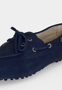 Mocassin bleu marine en daim avec nœud en lacets, œillets métalliques et doublure intérieure beige douce, doté d'une semelle noire texturée pour une bonne adhérence.